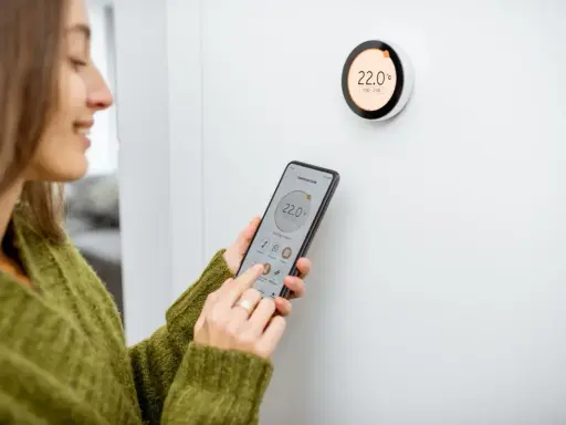 Donna controlla il termostato del riscaldamento tramite smartphone, mostrando come funziona il controllo intelligente della temperatura domestica.