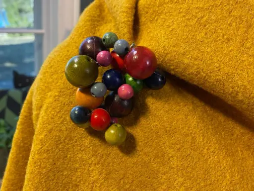 En gul, ullig poncho med en klunga av färgglada träpärlor som en brosch. Perfekt för att sy en unik poncho.