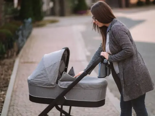 Młoda mama pochyla się nad szarym wózkiem dla dzieci, gotowa na spacer.
