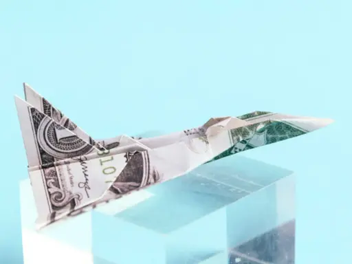 Ein **Flugzeug aus Geld falten** ist ein Kunstwerk. Ein Dollar-Schein wurde zu einem Jet gefaltet, der auf einem transparenten Block thront.