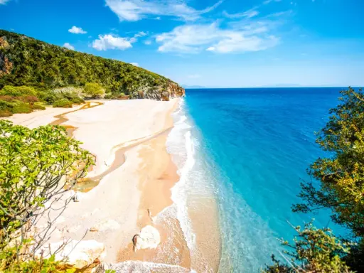 En orörd albanien strand med turkost vatten, vit sand och gröna kullar. En liten flod rinner ut i havet.
