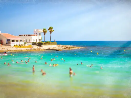 Sonnige Küste in Costa Calida, Spanien, mit vielen Menschen, die im türkisfarbenen Meer schwimmen.