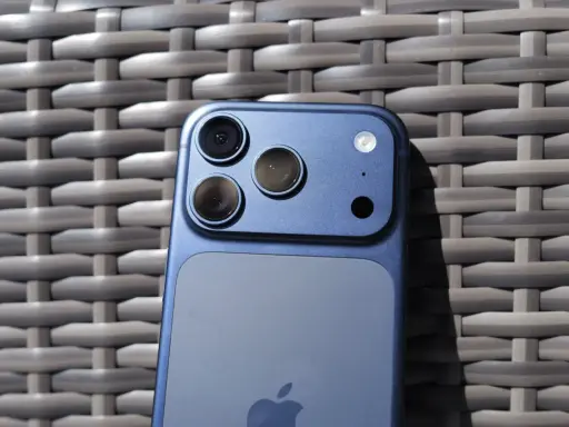 Niebieski iPhone 11 z potrójnym aparatem z tyłu, leżący na plecionej powierzchni.