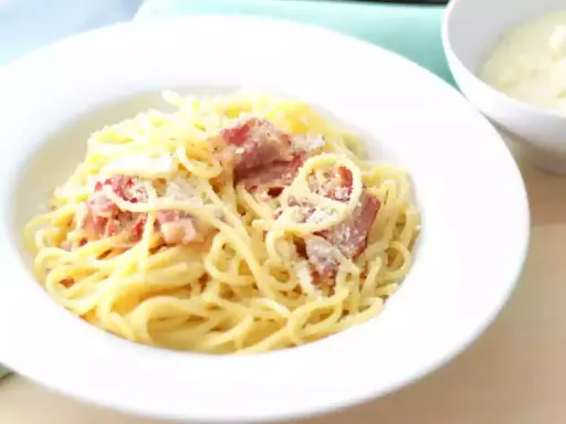Une assiette de spaghetti crémeux, parsemée de lardons et de parmesan. La vraie recette carbonara italienne, un délice simple et authentique.