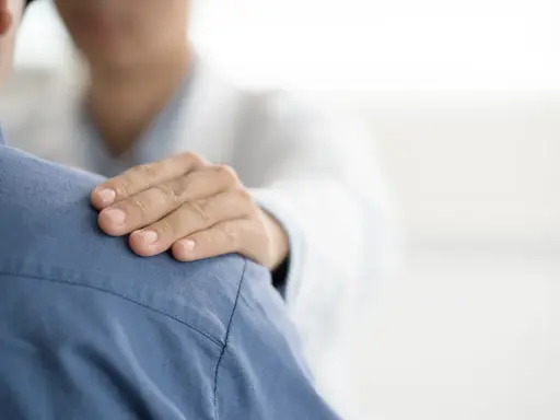 Dłoń lekarza na ramieniu pacjenta. Czy do psychiatry potrzebne jest skierowanie? Wsparcie i troska w gabinecie lekarskim.