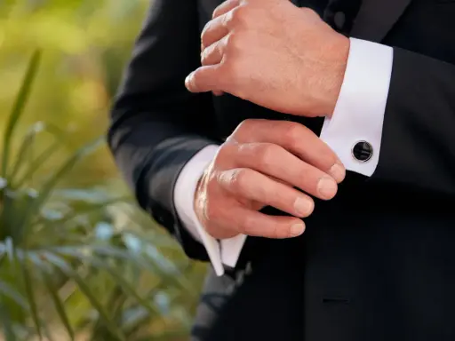 A man fastens his black cufflinks on his white shirt cuffs, completing his tux.