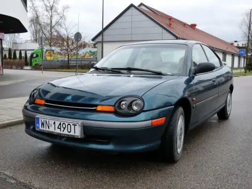 Zielony Dodge Neon z tablicą rejestracyjną WN 1490T stoi na mokrej drodze przed budynkiem.