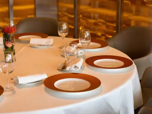 Une table dressée avec soin, des assiettes élégantes et des verres à moitié pleins, le tout dans une ambiance feutrée. L'art de la table est à l'honneur.