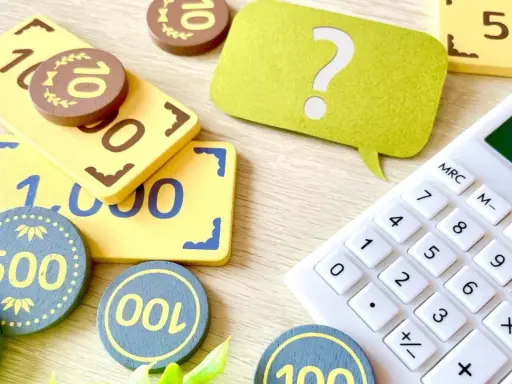 Jouets représentant des billets et des pièces, avec une calculatrice et un point d'interrogation. Une aide visuelle pour comprendre la fiscalité PEL.