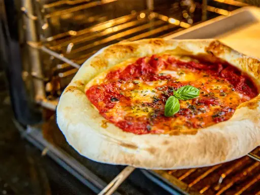 Leckere Pizza Margherita mit frischem Basilikum wird im Backofen gebacken. Der Teig ist goldbraun, die Tomatensauce blubbert.