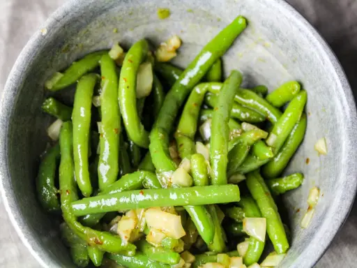 En skål med glansiga, gröna haricots verts blandade med bitar av vitlök och kryddor.