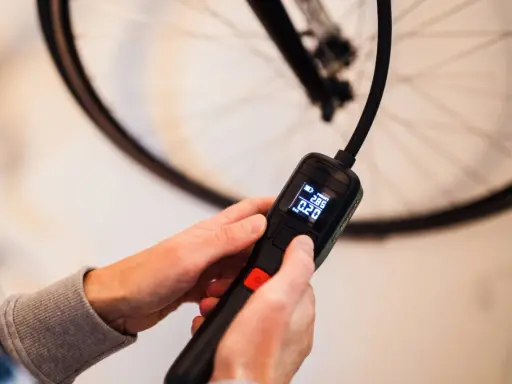 Hände halten eine digitale Luftpumpe, die den Druck in Bar anzeigt, bereit, den Fahrradreifen aufzufüllen.