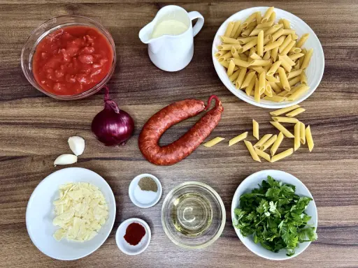 Składniki na pyszny makaron z chorizo: pomidory, cebula, czosnek, makaron penne, śmietanka, parmezan, oliwa, przyprawy i świeża natka pietruszki.