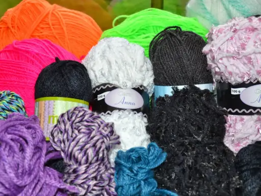 A colorful assortment of yarn balls in various textures and colors, including purple, pink, orange, green, white, black, and blue.