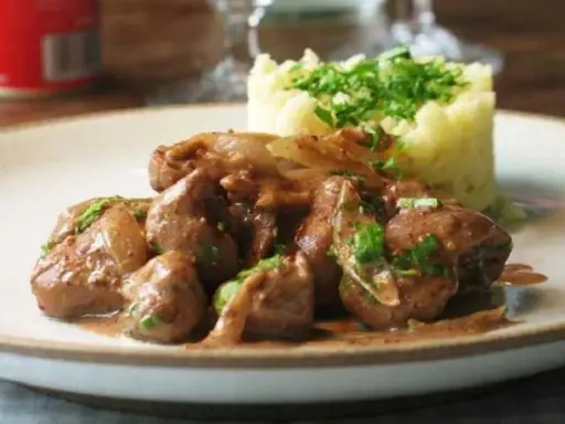 Une assiette de fricassée de rognons de veau, tendres et savoureux, accompagnés d'une purée de pommes de terre onctueuse et garnie de persil frais.