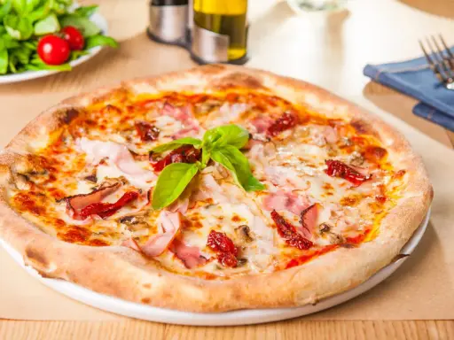 Une délicieuse pizza garnie de jambon, de tomates séchées et de champignons, avec une pousse de pâte à pizza bien dorée.