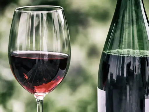 Ein Glas mit tiefrotem Zweigelt Rotwein steht neben einer grünen Flasche. Der Wein schimmert im Glas.