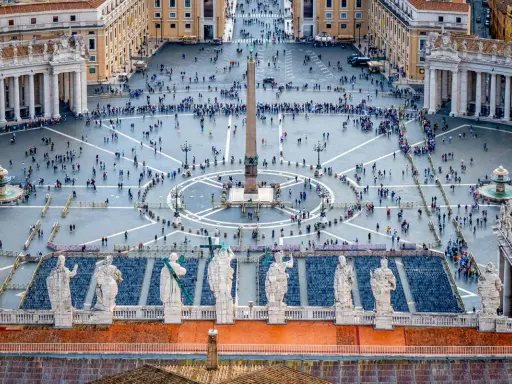 Vue aérienne de la **place du Vatican**, avec son obélisque central, ses fontaines et une foule de visiteurs.