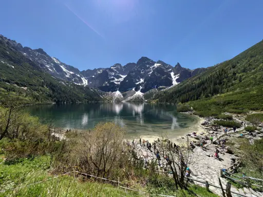 Widok na Morskie Oko z górami w tle i turystami na brzegu.