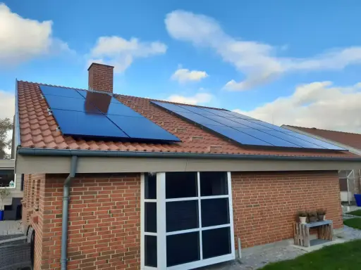 Ett tegelhus med solpaneler på taket, redo att generera egen energi. Blå himmel med vita moln.