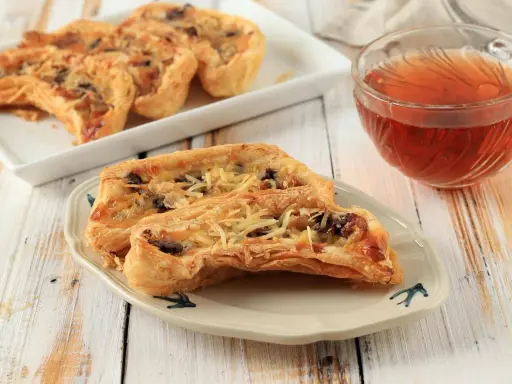 Pyszny obiad z ciasta francuskiego, chrupiące kawałki z serem i nadzieniem, obok filiżanka herbaty.