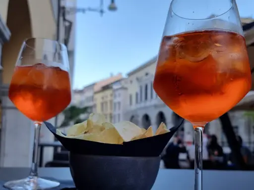Dwa drinki Aperol Spritz i miseczka chipsów na stoliku. Czy alkohol podnosi cholesterol? To pytanie zadaje sobie wielu, delektując się takimi przekąskami.