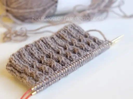 Knitted swatch with textured pattern and yarn on needles.