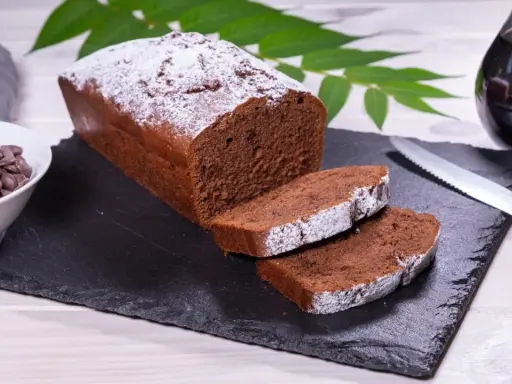 Ein saftiger Schokoladenkuchen, bestäubt mit Puderzucker, bereit für ein köstliches rotweinkuchen rezept. Daneben Schokoladendrops und ein Glas Rotwein.