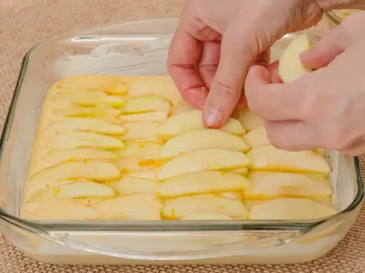 Ręce układają plasterki jabłek na cieście. Powstaje pyszne ciasto z jabłkami, gotowe do pieczenia.