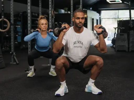 Mann und Frau trainieren Kraftsport mit Kettlebells im Fitnessstudio.