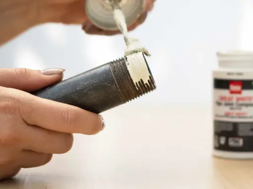 Application de pâte sur le filetage d'un **tube pour joint**. Un pot de pâte est visible à droite.