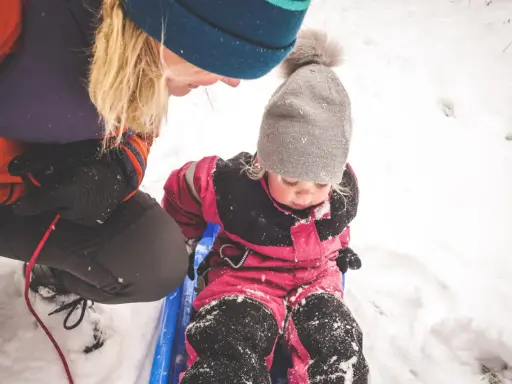 En vuxen drar ett barn på en pulka i snön. Ett perfekt exempel på friluftsliv barn.