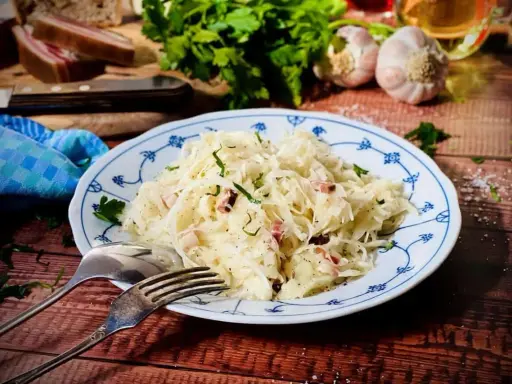 Ein Teller mit Krautsalat, garniert mit Petersilie. Daneben liegen Gabel und Löffel. Ein leckeres Krautsalat Rezept für dich!