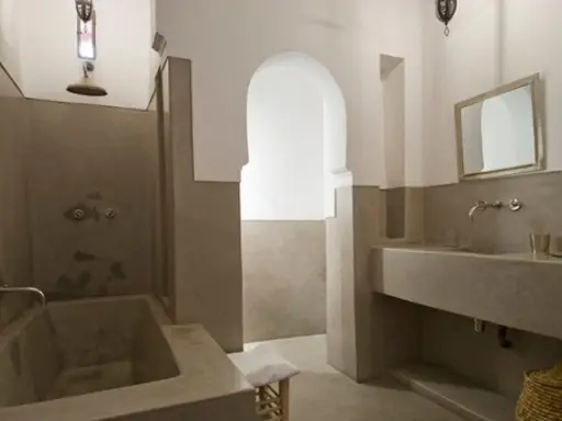 Modernes Badezimmer mit einer freistehenden Badewanne und einem Waschbecken aus Tadelakt. Ein großer Spiegel und ein traditioneller Korb vervollständigen den Look.