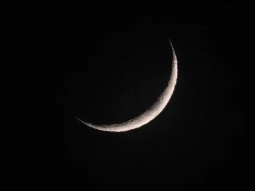 Eine schmale Mondsichel leuchtet im dunklen Nachthimmel. Sie erinnert an den Beginn von Ramadan, wann die Zeit des Fastens beginnt.