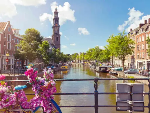 Das **beste von Amsterdam**: malerischer Kanal mit Booten, historischen Gebäuden und einem Kirchturm. Blumenverzierte Fahrräder auf einer Brücke.