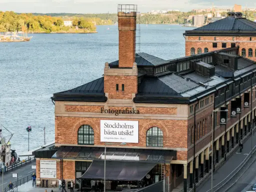 Fotografiska Stockholm vid vattnet, med en båt i förgrunden och en stadssilhuett i bakgrunden.