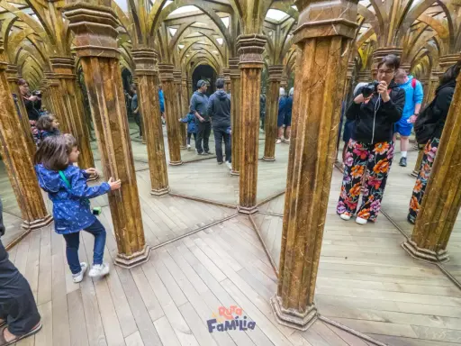 Niños exploran un laberinto de espejos con columnas doradas, creando un divertido juego de "praga con niños" y reflejos infinitos.