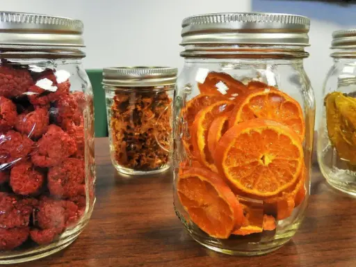Vier Gläser mit getrockneten Früchten: Himbeeren, Orangenscheiben, etwas Braunes und etwas Gelbes. Perfekt zum glas beschriften für die Vorratshaltung.