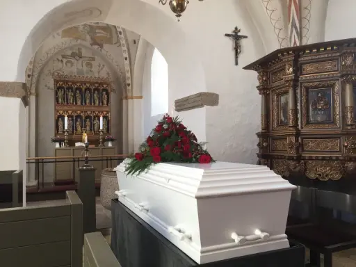 Biała trumna z czerwonymi różami w kościele. Warto wiedzieć, jak się zachować przy otwartej trumnie, by okazać szacunek zmarłemu.