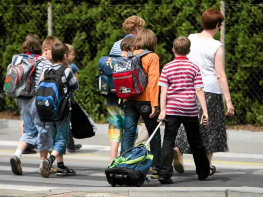 Niños con mochilas y un carrito cruzan la calle, marcando el regreso a la rutina de septiembre.