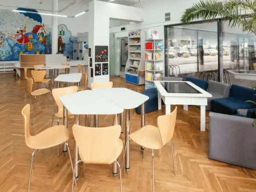 Spazi della scuola luminosi con scaffali, tavoli, sedie e un murale colorato. Un'area accogliente per imparare e giocare.