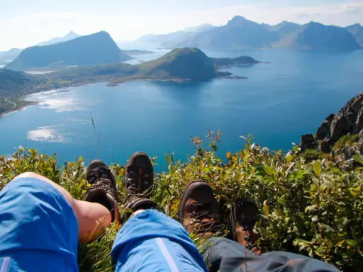 Vandringsskor vilar på en grön sluttning med en fantastisk utsikt över havet och bergen på Lofoten sommar.