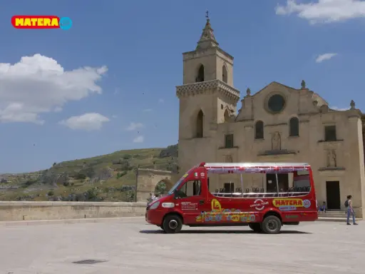 Un bus rosso "open top" per un tour di Matera, con la chiesa e i Sassi sullo sfondo.