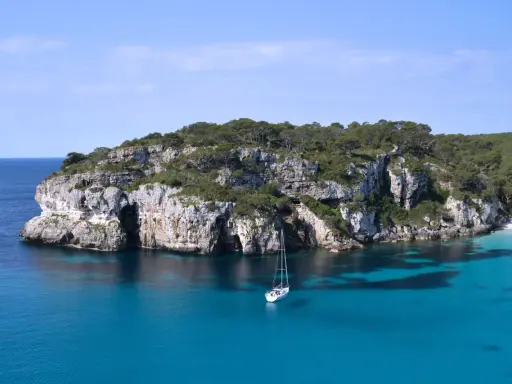 Żaglówka kołysze się na turkusowych wodach u wybrzeży skalistej zatoczki. To krajobraz z największej wyspy balearów, gdzie przyroda zachwyca.