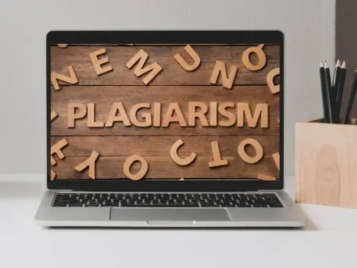 Laptop z napisem "PLAGIARISM" ułożonym z drewnianych liter na tle desek.