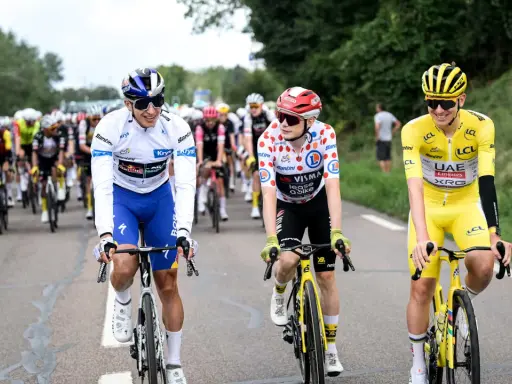 Radfahrer in bunten Trikots, Teil der Tour de France Teams, fahren auf der Straße. Einer trägt das Gelbe Trikot.