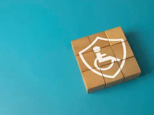 Drewniane klocki tworzą tarczę z symbolem osoby na wózku inwalidzkim. To symbol tego, co daje orzeczenie o niepełnosprawności – wsparcie i ochronę.
