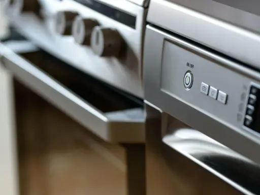 Nowoczesna kuchnia z piekarnikiem i zmywarką obok. Panel sterowania zmywarki z przyciskiem ON/OFF.