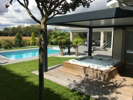 Un spa bouillonnant sur une terrasse en bois, à côté d'une piscine bleue. Le tableau temps de filtration piscine est visible dans le jardin luxuriant.